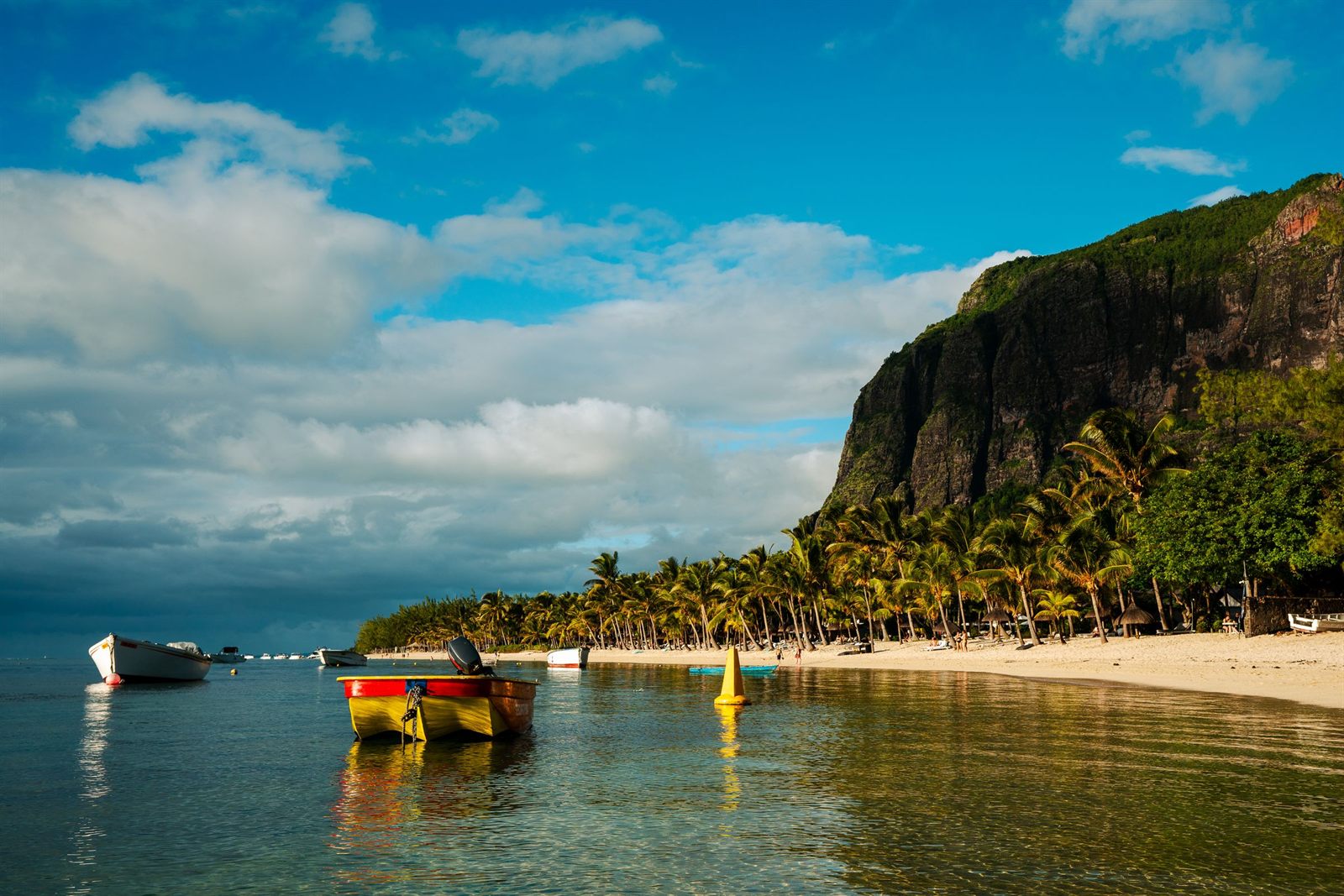 Small boats moored off a beach below a steep green headland in Mauritius