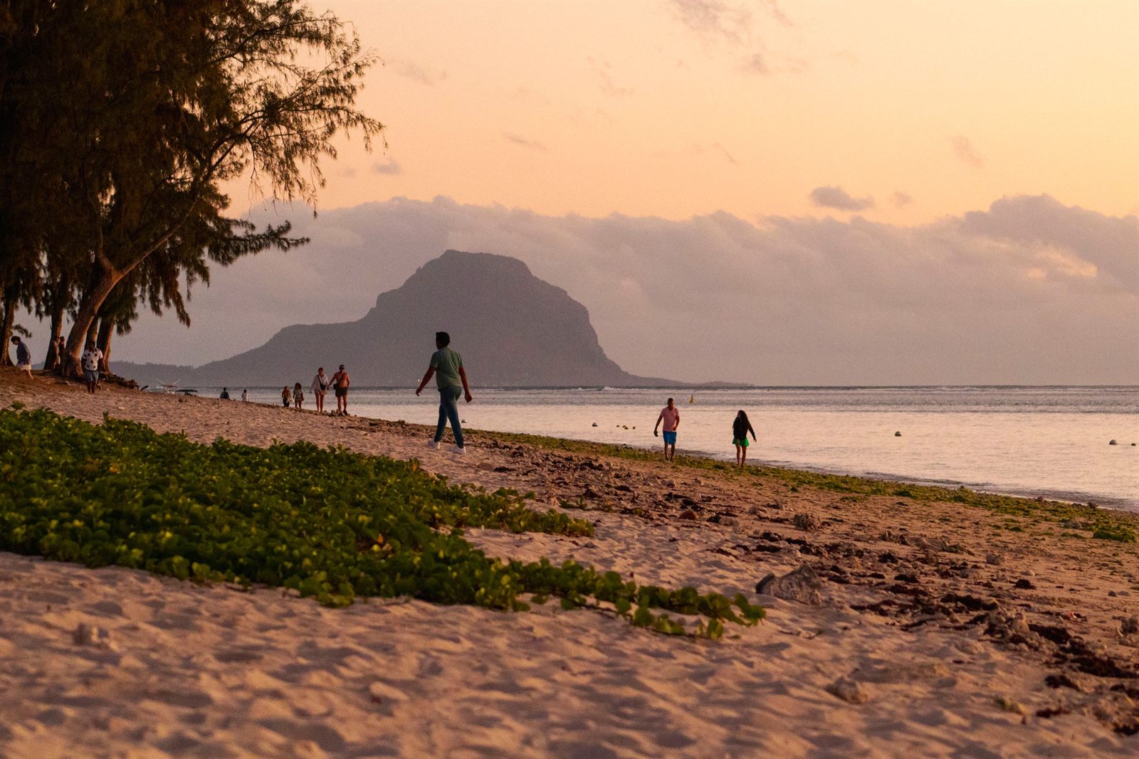 People walking along a beach at sunset with a mountain across the bay